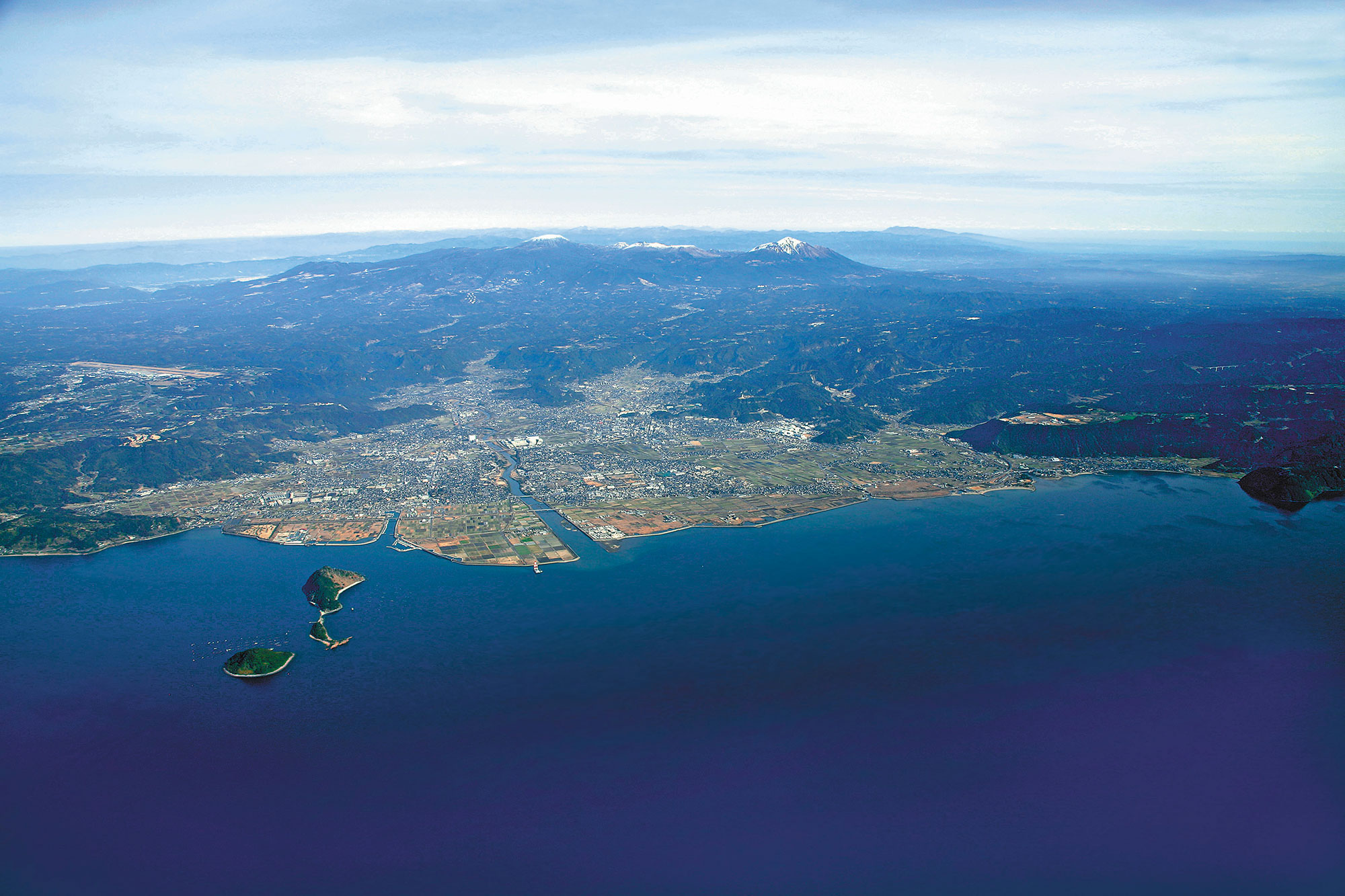 錦江湾（鹿児島湾）上空から見る霧島山とそのふもとに広がる霧島市。霧島市は、錦江湾の標高0ｍから韓国岳の山頂まで1700ｍの標高差をもつ。